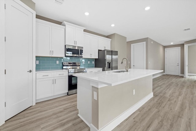 kitchen with appliances with stainless steel finishes, light wood-type flooring, a center island with sink, and sink