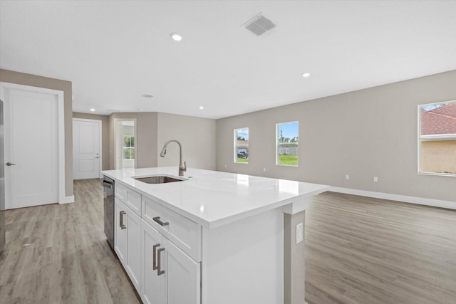 kitchen featuring a kitchen island with sink, sink, light hardwood / wood-style flooring, dishwasher, and white cabinetry