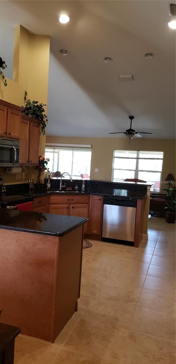 kitchen with light tile patterned floors, appliances with stainless steel finishes, ceiling fan, dark stone counters, and sink