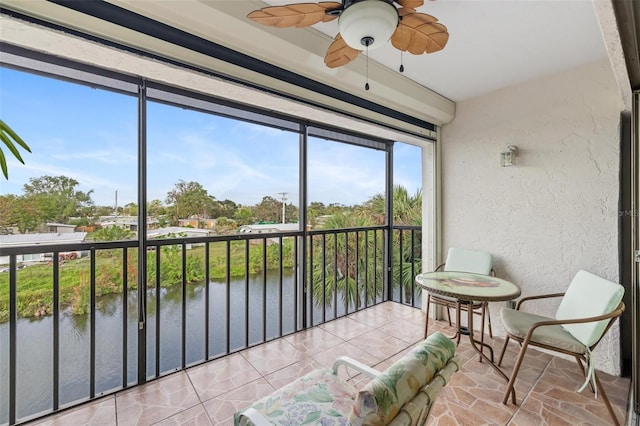 sunroom with ceiling fan and a water view