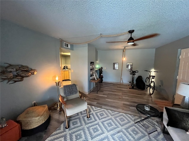 living area featuring a textured ceiling, hardwood / wood-style flooring, and ceiling fan