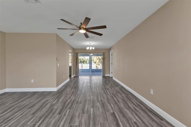 spare room featuring dark wood-type flooring, ceiling fan with notable chandelier, and baseboards