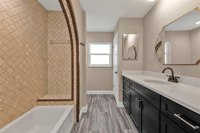 bathroom with baseboards, wood tiled floor, a garden tub, tiled shower, and vanity