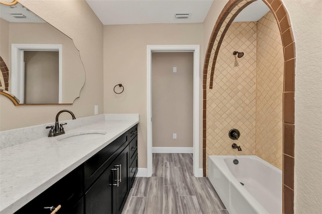 bathroom featuring vanity, washtub / shower combination, baseboards, visible vents, and wood finish floors