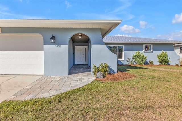 doorway to property featuring a yard, stucco siding, metal roof, and a garage