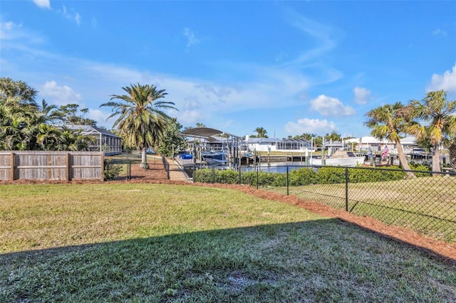 view of yard featuring fence, a water view, and a boat dock