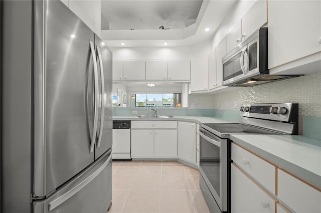 kitchen featuring stainless steel appliances, light tile patterned flooring, sink, tasteful backsplash, and white cabinets