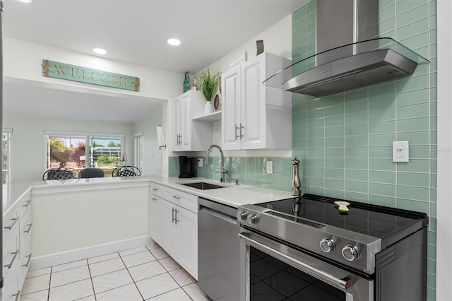 kitchen featuring a sink, white cabinets, wall chimney range hood, appliances with stainless steel finishes, and backsplash