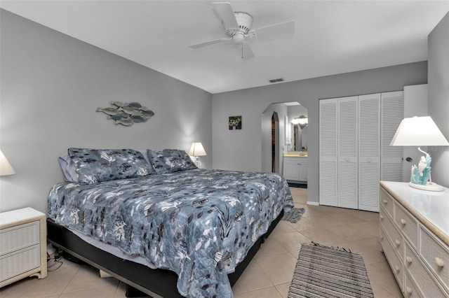 bedroom with light tile patterned flooring, connected bathroom, ceiling fan, and a closet