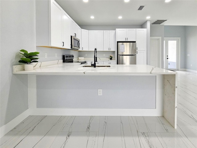 kitchen with appliances with stainless steel finishes, kitchen peninsula, white cabinets, and sink