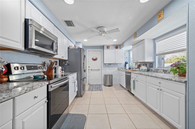 kitchen featuring appliances with stainless steel finishes, light tile patterned flooring, ceiling fan, white cabinets, and light stone counters