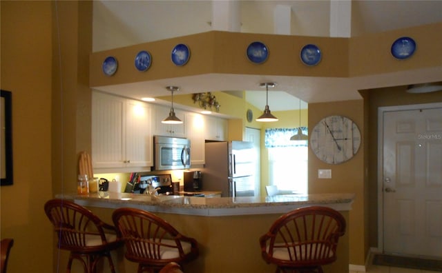 kitchen with appliances with stainless steel finishes, kitchen peninsula, hanging light fixtures, a kitchen breakfast bar, and light stone counters