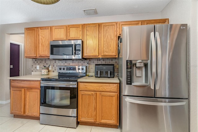 kitchen with a textured ceiling, light tile patterned floors, backsplash, and appliances with stainless steel finishes