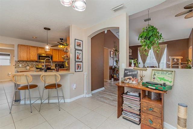 kitchen featuring backsplash, a kitchen bar, light tile patterned floors, kitchen peninsula, and ceiling fan