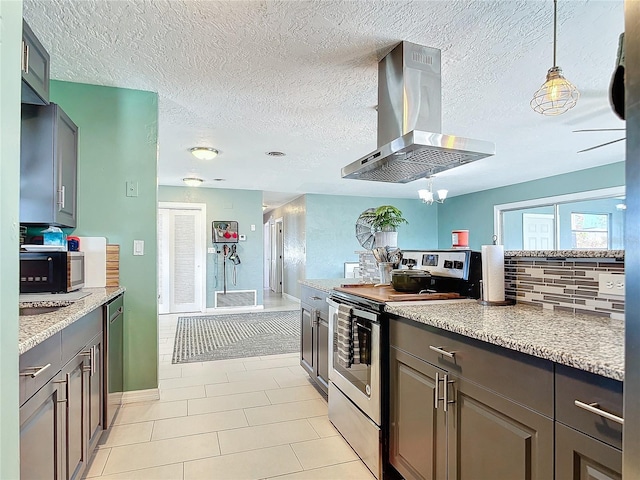 kitchen with wall chimney range hood, stainless steel appliances, light tile patterned floors, light stone counters, and a textured ceiling