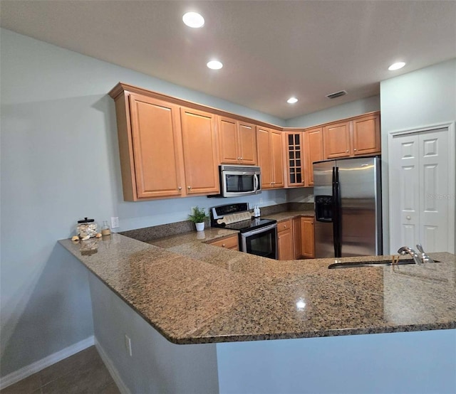 kitchen with dark stone countertops, glass insert cabinets, a sink, stainless steel appliances, and recessed lighting