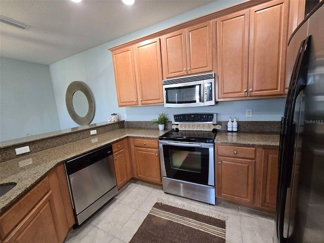kitchen featuring dark stone countertops, light tile patterned floors, appliances with stainless steel finishes, and brown cabinets