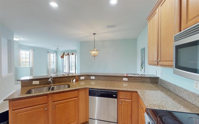 kitchen with light stone counters, a sink, stainless steel appliances, decorative light fixtures, and a peninsula