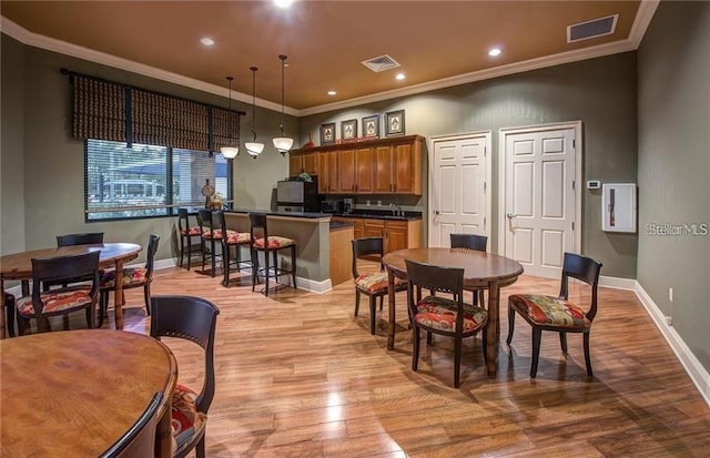 dining area with crown molding, light wood finished floors, visible vents, and baseboards