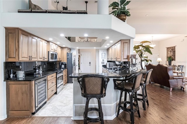 kitchen with kitchen peninsula, appliances with stainless steel finishes, light wood-type flooring, beverage cooler, and a tray ceiling