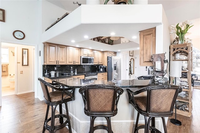 kitchen with dark stone countertops, light wood-type flooring, kitchen peninsula, and stainless steel appliances