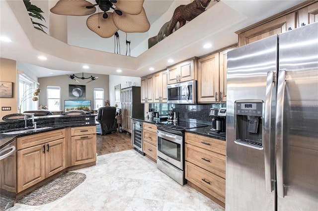 kitchen featuring sink, appliances with stainless steel finishes, ceiling fan, dark stone countertops, and beverage cooler