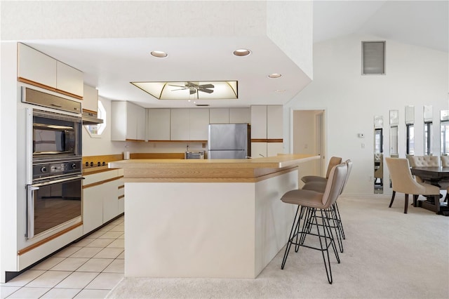 kitchen with white cabinetry, light carpet, vaulted ceiling, stainless steel refrigerator, and a breakfast bar area