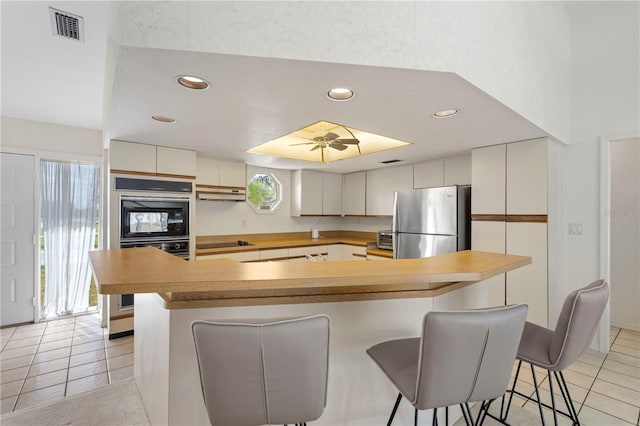 kitchen with a breakfast bar area, a large island, black appliances, light tile patterned floors, and ceiling fan