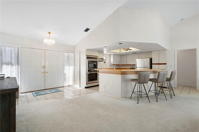 kitchen with stainless steel fridge, a breakfast bar area, white cabinetry, black double oven, and light colored carpet