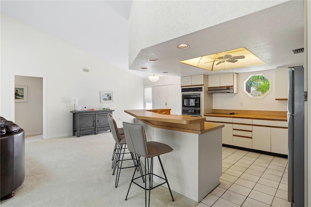 kitchen with light carpet, black appliances, a breakfast bar area, and ceiling fan