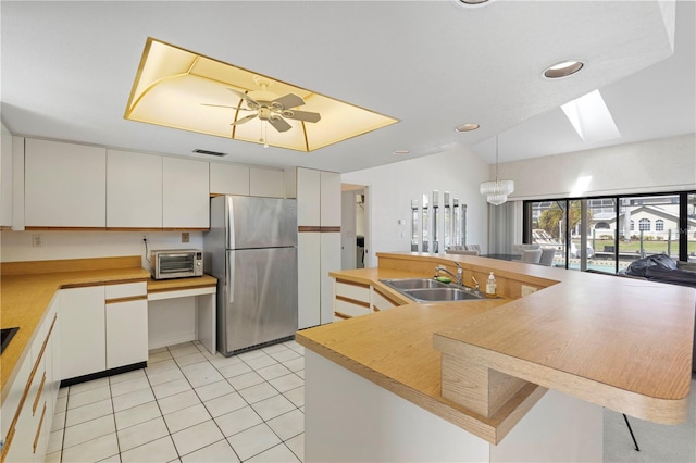 kitchen featuring white cabinetry, stainless steel refrigerator, ceiling fan with notable chandelier, a skylight, and sink