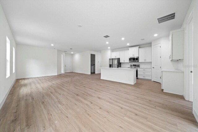 kitchen with a kitchen island with sink, stainless steel appliances, white cabinetry, light hardwood / wood-style floors, and tasteful backsplash