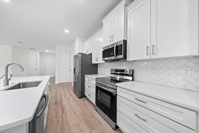 kitchen featuring sink, backsplash, stainless steel appliances, white cabinets, and light hardwood / wood-style flooring