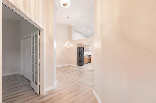 hall featuring high vaulted ceiling, light hardwood / wood-style flooring, and an inviting chandelier