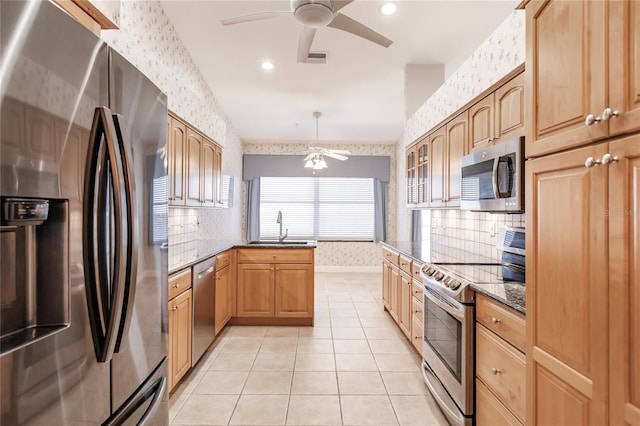 kitchen with stainless steel appliances, dark stone counters, hanging light fixtures, sink, and ceiling fan