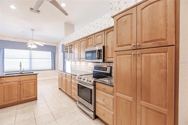 kitchen with dark stone counters, sink, ceiling fan, light tile patterned flooring, and appliances with stainless steel finishes