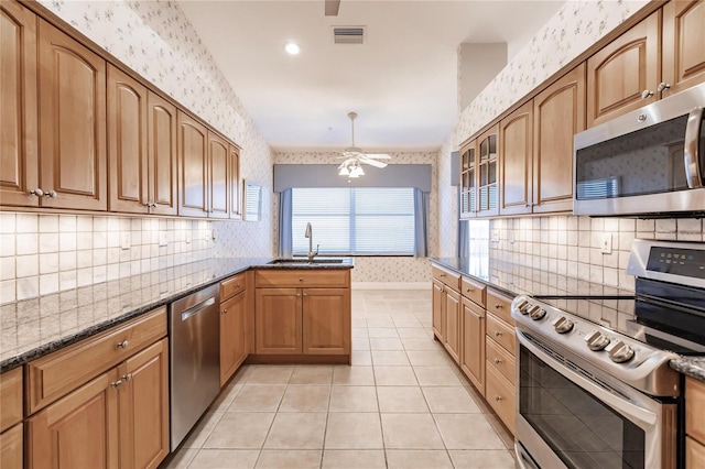 kitchen featuring stainless steel appliances, dark stone counters, sink, and light tile patterned flooring