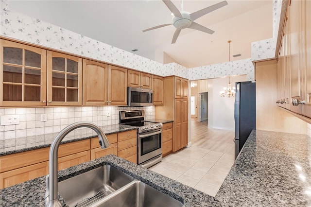 kitchen with light wood-type flooring, appliances with stainless steel finishes, dark stone counters, and sink