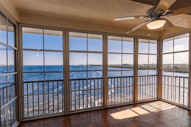 unfurnished sunroom with plenty of natural light, a water view, and ceiling fan