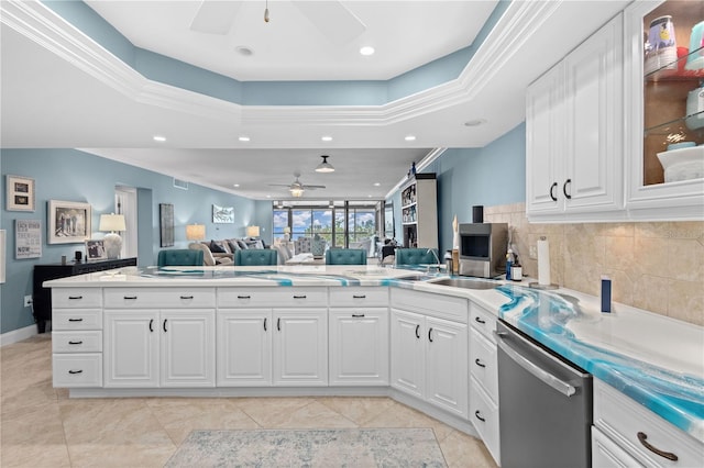 kitchen with a tray ceiling, backsplash, crown molding, stainless steel dishwasher, and white cabinets