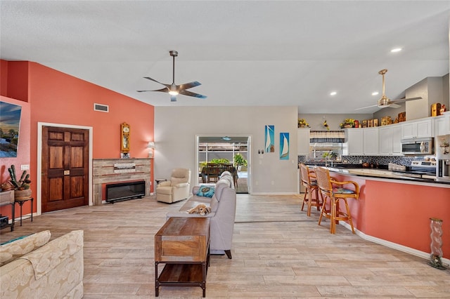 living room with a fireplace, ceiling fan, light wood-type flooring, and vaulted ceiling