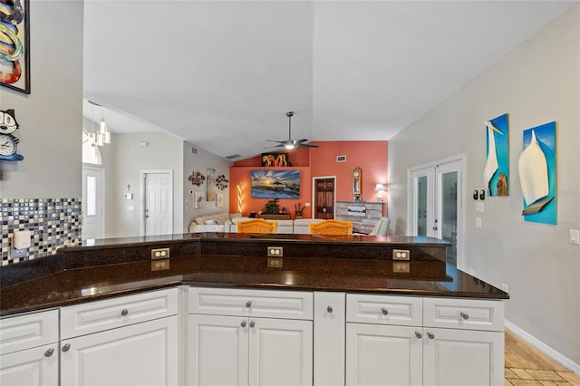 kitchen with dark stone counters, white cabinetry, lofted ceiling, and ceiling fan with notable chandelier