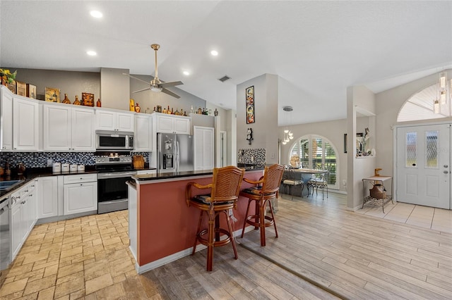 kitchen featuring stainless steel appliances, ceiling fan with notable chandelier, white cabinets, and a breakfast bar