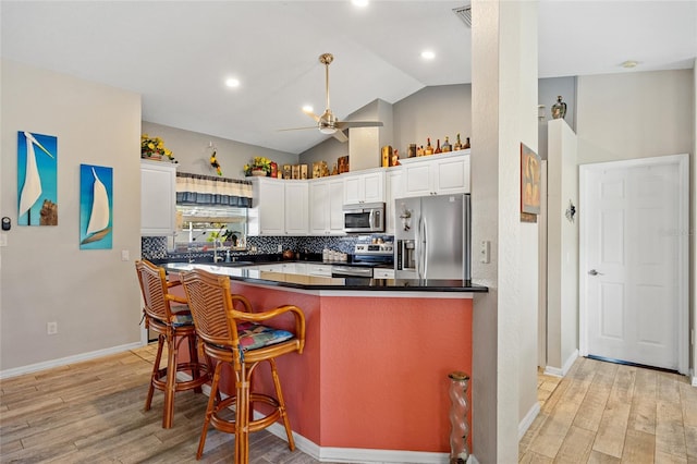 kitchen featuring backsplash, appliances with stainless steel finishes, vaulted ceiling, white cabinets, and light hardwood / wood-style flooring