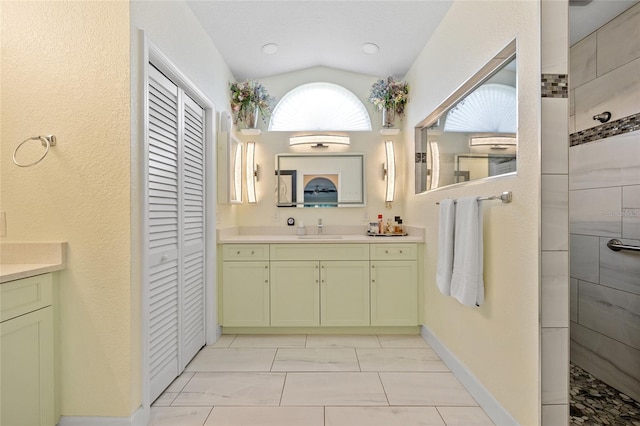 bathroom with vanity, tiled shower, and lofted ceiling