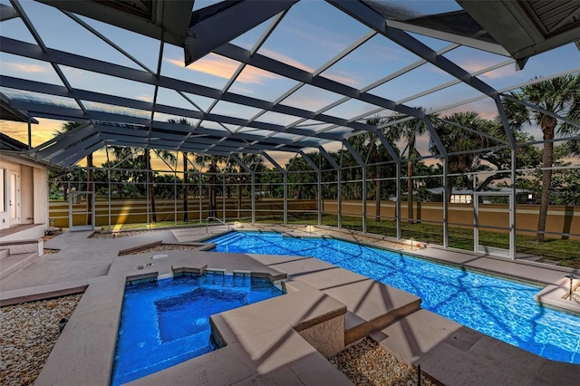 pool at dusk with an in ground hot tub, a patio area, and a lanai