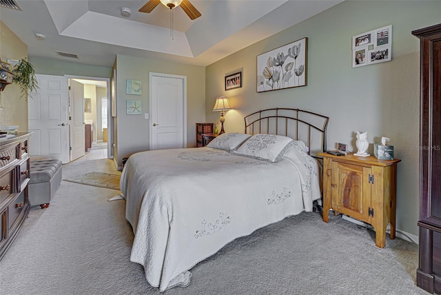 bedroom featuring light carpet, ensuite bathroom, a tray ceiling, and ceiling fan