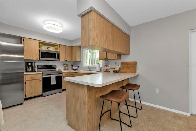 kitchen featuring light brown cabinetry, kitchen peninsula, appliances with stainless steel finishes, and a kitchen bar