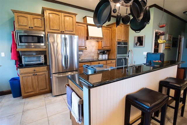 kitchen featuring decorative backsplash, a kitchen island with sink, stainless steel appliances, crown molding, and light tile patterned flooring