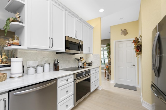 kitchen with tasteful backsplash, appliances with stainless steel finishes, light wood-type flooring, and white cabinets